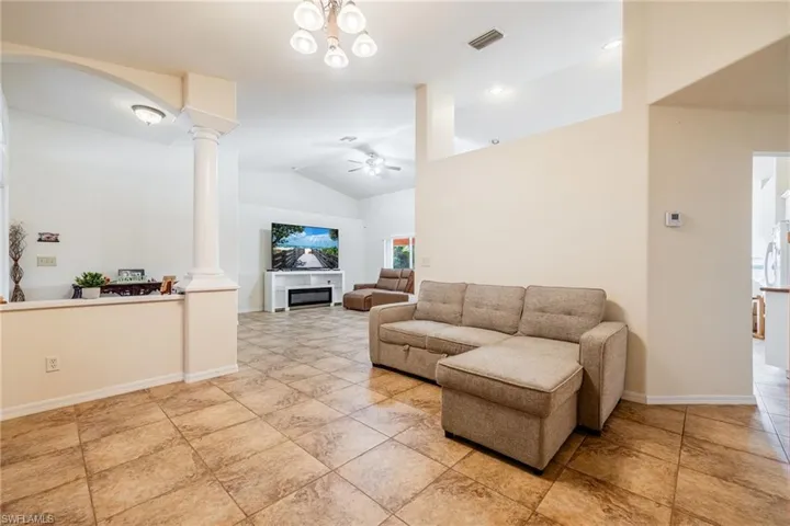 Living area 2 with ceiling fan, visible vents, baseboards, vaulted ceiling, and decorative columns