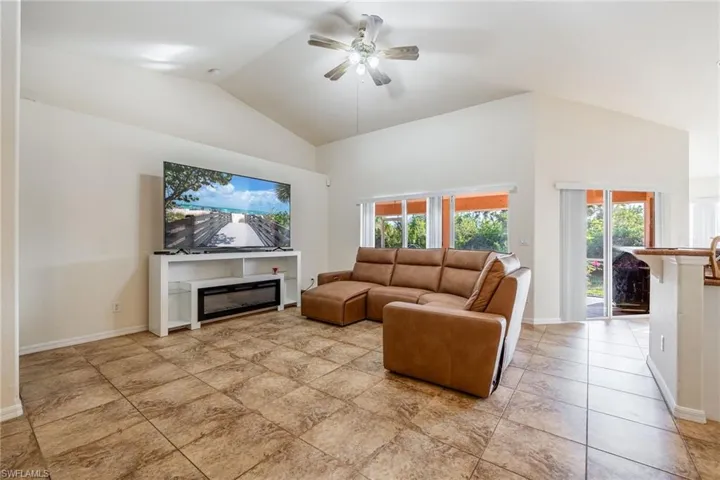 Living area featuring ceiling fan, high vaulted ceiling, a glass covered fireplace, and baseboards