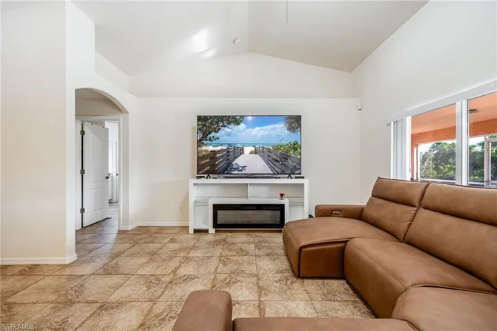 Living room with arched walkways, a glass covered fireplace, lofted ceiling, and baseboards