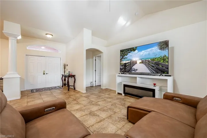 Living room with lofted ceiling, decorative columns, arched walkways, and baseboards