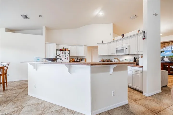 Kitchen featuring a breakfast bar area, visible vents, white microwave, a kitchen island with sink, and white cabinets