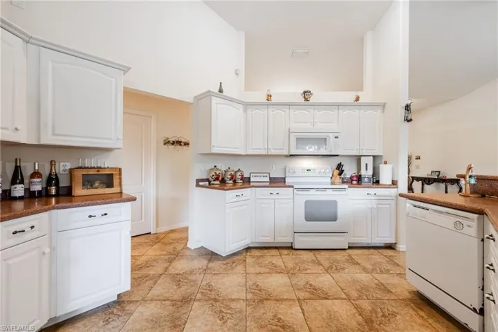 Kitchen with dark countertops, white appliances, and white cabinetry