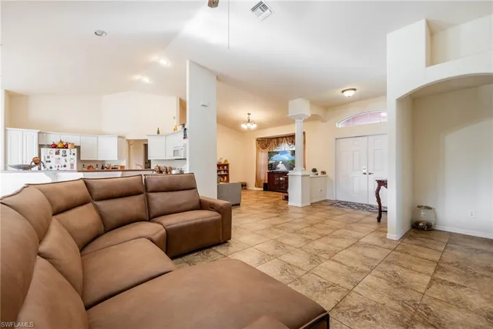 Living room with high vaulted ceiling, decorative columns, visible vents, and baseboards