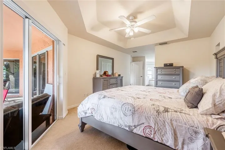 Bedroom with ceiling fan, light carpet, visible vents, baseboards, and a raised ceiling