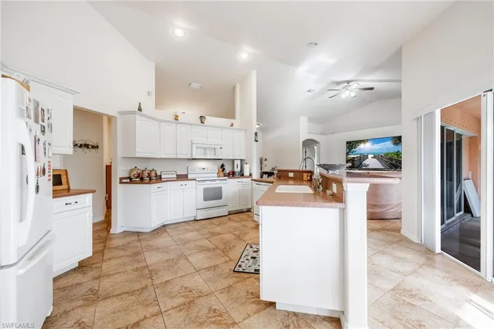 Kitchen featuring white appliances, a ceiling fan, open floor plan, white cabinetry, and a sink
