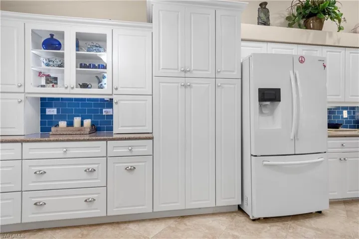 Kitchen with decorative backsplash, white cabinetry, white French-door refrigerator and quartz countertops