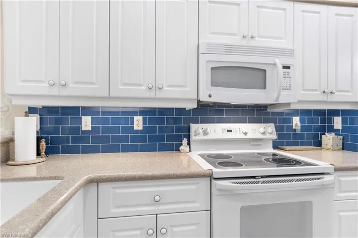 Kitchen with white appliances, quartz countertops, white cabinets, and subway tile backsplash.