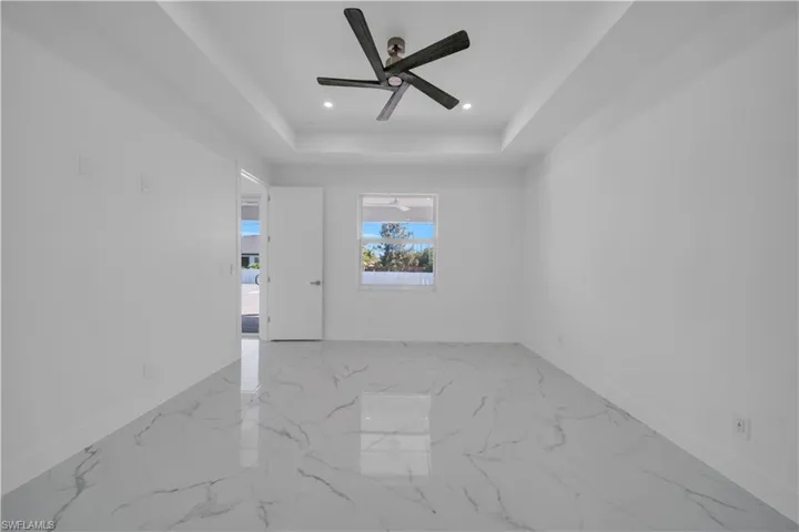 Unfurnished room with ceiling fan, light marble finish flooring, a tray ceiling, and recessed lighting
