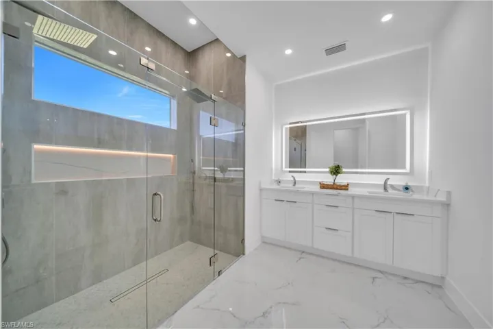 Full bathroom featuring double vanity, a marble finish shower, light marble finish flooring, and recessed lighting