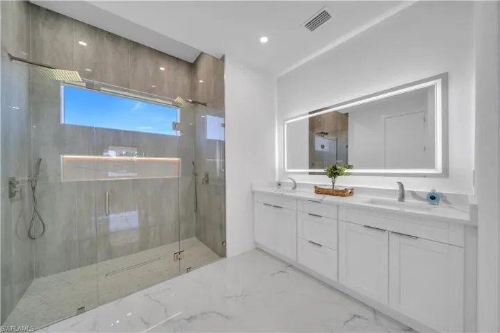 Bathroom featuring double vanity, a marble finish shower, light marble finish flooring, and recessed lighting