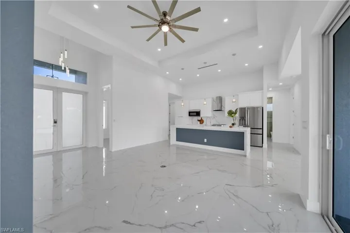 Unfurnished living room featuring a high ceiling, recessed lighting, ceiling fan, light marble finish flooring, and french doors