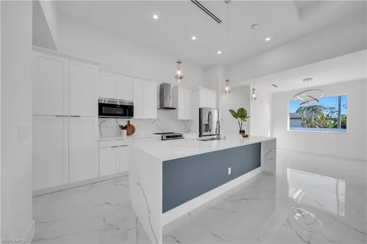Kitchen featuring white cabinets, light stone counters, hanging light fixtures, and stainless steel appliances