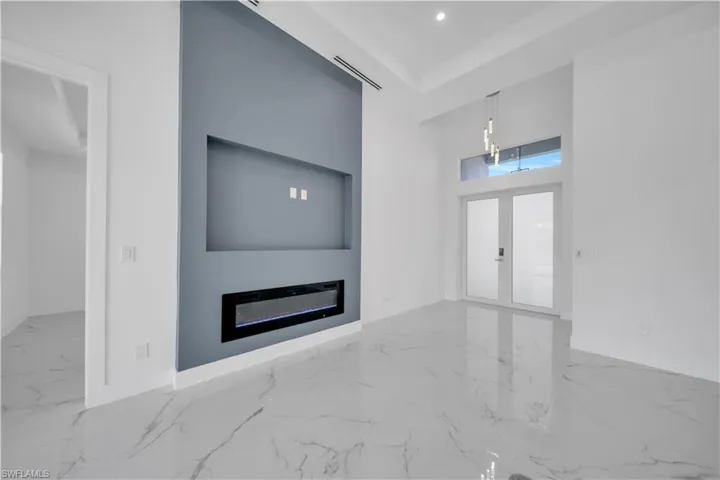 Unfurnished living room with a high ceiling, french doors, a glass covered fireplace, light marble finish floors, and recessed lighting