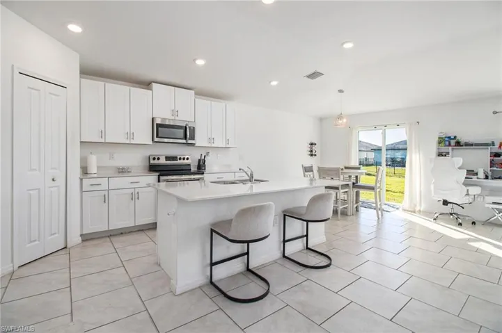 Kitchen with white cabinetry, appliances with stainless steel finishes, a breakfast bar, decorative light fixtures, and recessed lighting