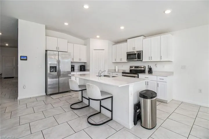Kitchen with appliances with stainless steel finishes, white cabinets, vaulted ceiling, a kitchen bar, and a kitchen island with sink