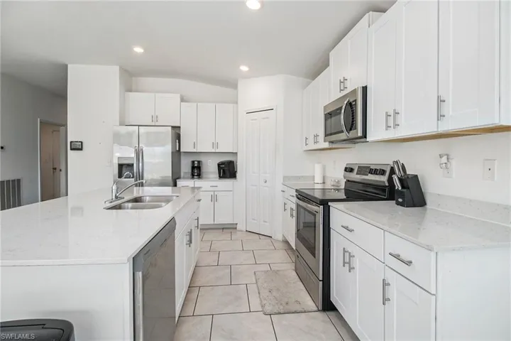 Kitchen with appliances with stainless steel finishes, a center island with sink, white cabinets, light stone countertops, and light tile patterned floors