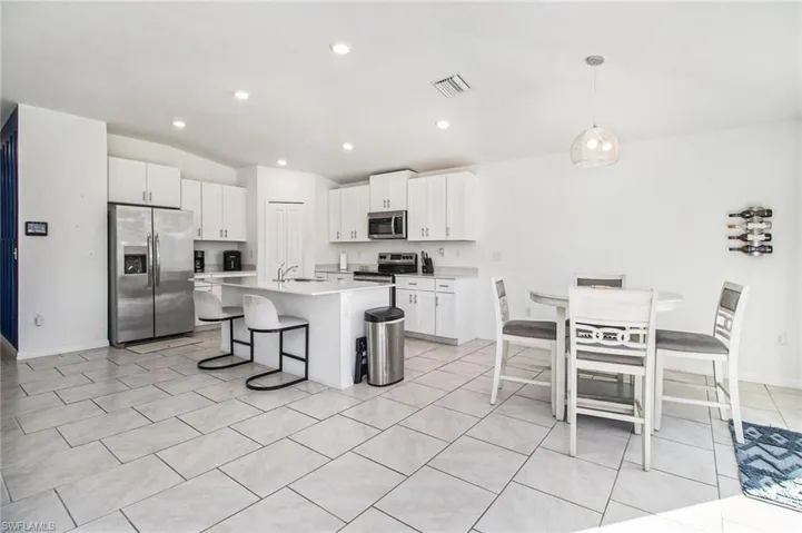 Kitchen featuring stainless steel appliances, a kitchen bar, white cabinetry, a kitchen island with sink, and lofted ceiling