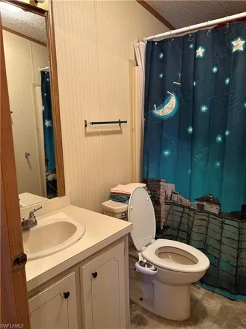 Bathroom with a textured ceiling, vanity, and toilet
