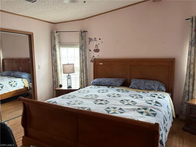 Bedroom with a textured ceiling, wood-type flooring, lofted ceiling, and ornamental molding