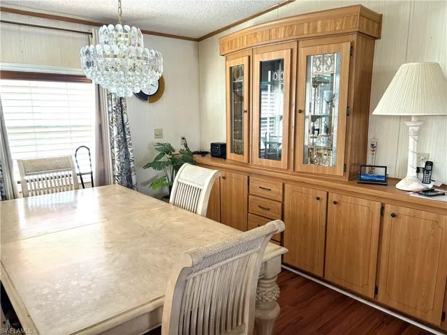 Dining area featuring an inviting chandelier, a textured ceiling, crown molding, and dark hardwood / wood-style flooring