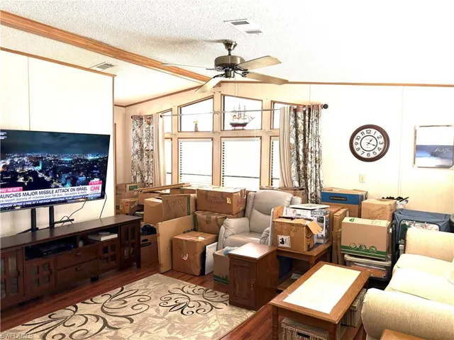 Living room with a textured ceiling, lofted ceiling, ceiling fan, light hardwood / wood-style flooring, and ornamental molding
