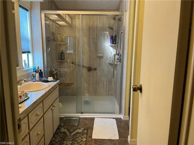Bathroom with a textured ceiling, vanity, and a shower with shower door
