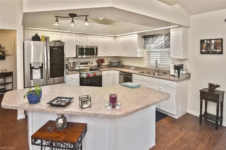 Kitchen with appliances with stainless steel finishes, white cabinetry, light countertops, dark wood-style flooring, and a kitchen breakfast bar