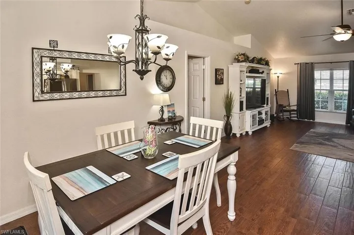Dining area featuring vaulted ceiling, wood-style floors, a chandelier, and a ceiling fan