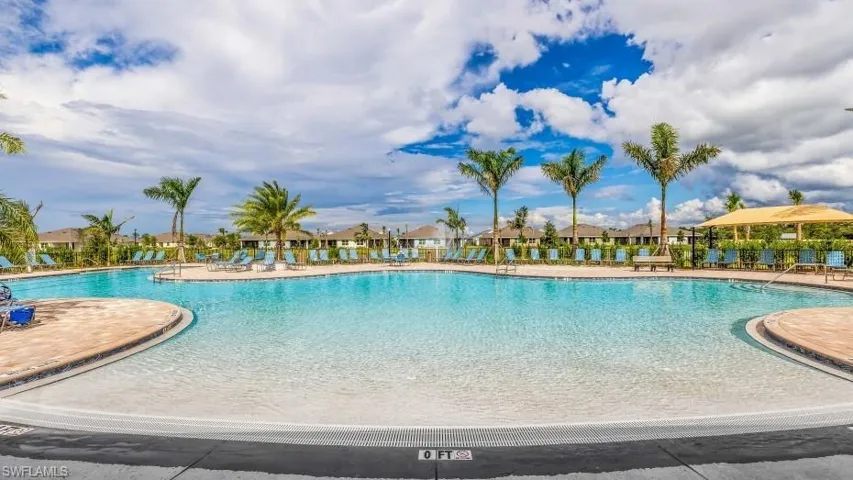 Expansive community swimming pool with ashallow entry area, surrounded by palm trees and lounge chairs