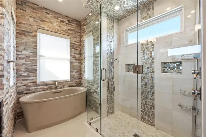 Another view of main bath tub and shower with dual controls and shower heads, extensive tilework,and insets