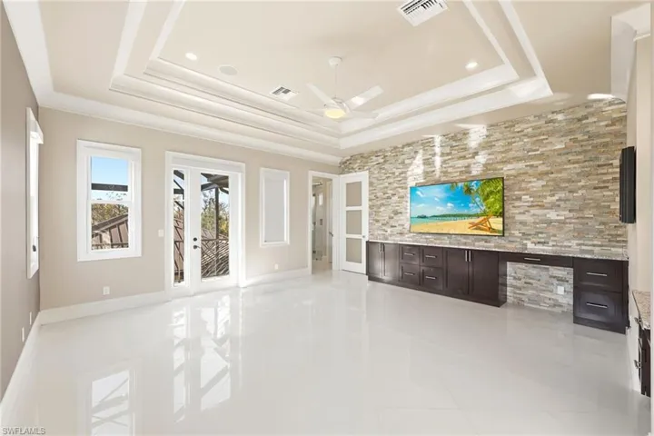 Main bedroom with custom stonework,dresser space, and tray ceiling  leading to balcony