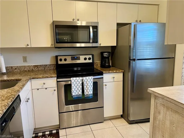 Kitchen featuring stone counters, appliances with stainless steel finishes, sink, white cabinets, and light tile patterned floors