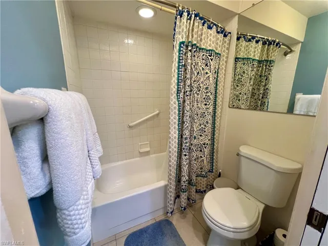Bathroom with shower / bathtub combination with curtain, tile patterned floors, and toilet