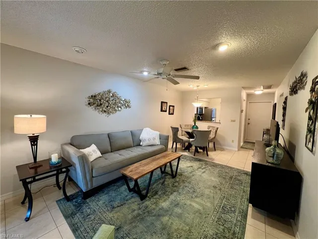 Living room with ceiling fan, a textured ceiling, and light tile patterned flooring