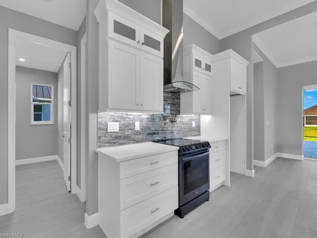 Kitchen featuring electric range, wall chimney range hood, decorative backsplash, glass insert cabinets, and light countertops