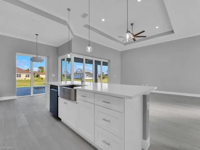 Kitchen with ceiling fan, a raised ceiling, light countertops, a kitchen island with sink, and healthy amount of natural light