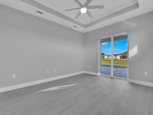 Empty room featuring a tray ceiling, ceiling fan, and wood finished floors