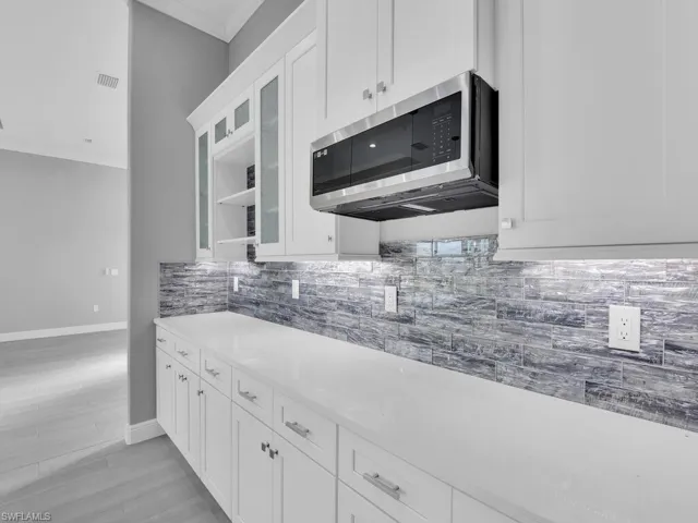 Kitchen featuring stainless steel microwave, backsplash, white cabinets, and glass insert cabinets