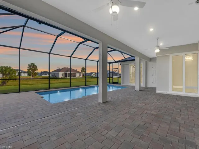 Pool at dusk with an outdoor pool, ceiling fan, a patio, and a lawn
