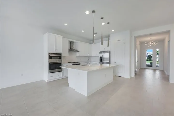 Kitchen with appliances with stainless steel finishes, an island with sink, wall chimney exhaust hood, with view of Foyer including chandelier