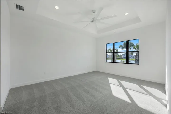 Primary bedroom with carpet, ceiling fan, and a raised ceiling
