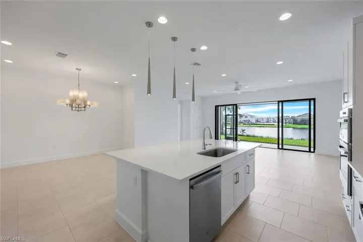 Kitchen with white cabinets, an island with sink, stainless steel dishwasher, and views of Dining Room, Living Room and Lanai with water views