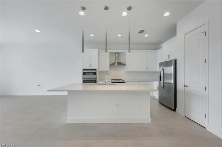 Kitchen featuring stainless steel appliances, a center island with sink, wall chimney exhaust hood, and white cabinets