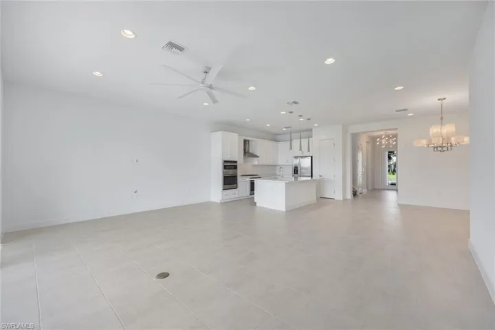 Living room featuring ceiling fan with views of dining room with notable chandelier and kitchen with pendant lighting
