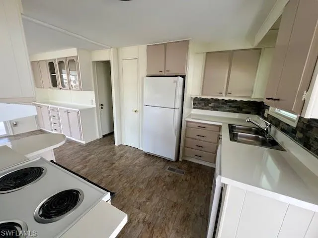 Kitchen featuring dark wood-type flooring, tasteful backsplash, a sink, and white appliances