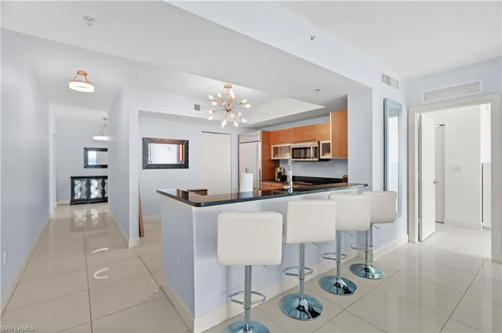 Kitchen featuring brown cabinetry, a kitchen bar, light tile patterned floors, a peninsula, and a chandelier
