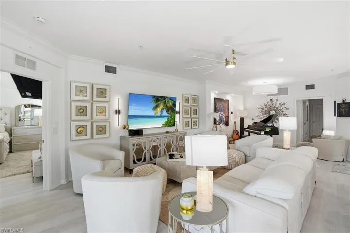 Spacious living area featuring light wood-finish flooring, a contemporary ceiling fan with gold-tone accents, recessed lighting, and crown molding
