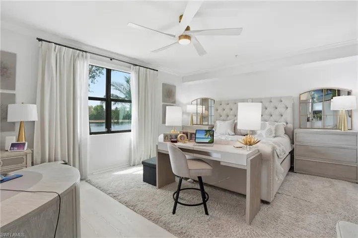 Spacious interior featuring a large window with a water backdrop, a contemporary ceiling fan, light-toned walls, crown molding, and wood-finish flooring