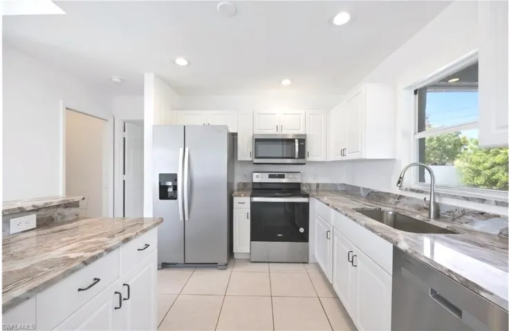 Kitchen with appliances with stainless steel finishes, light stone countertops, white cabinets, light tile patterned floors, and sink