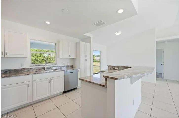 Kitchen featuring light tile patterned floors, sink, white cabinetry, stainless steel dishwasher, and kitchen peninsula